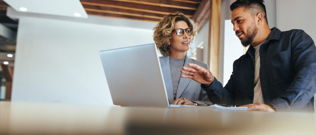 Business man having a discussion with his colleague in an office. Two business people using a laptop in a meeting. Teamwork and collaboration between business professionals.